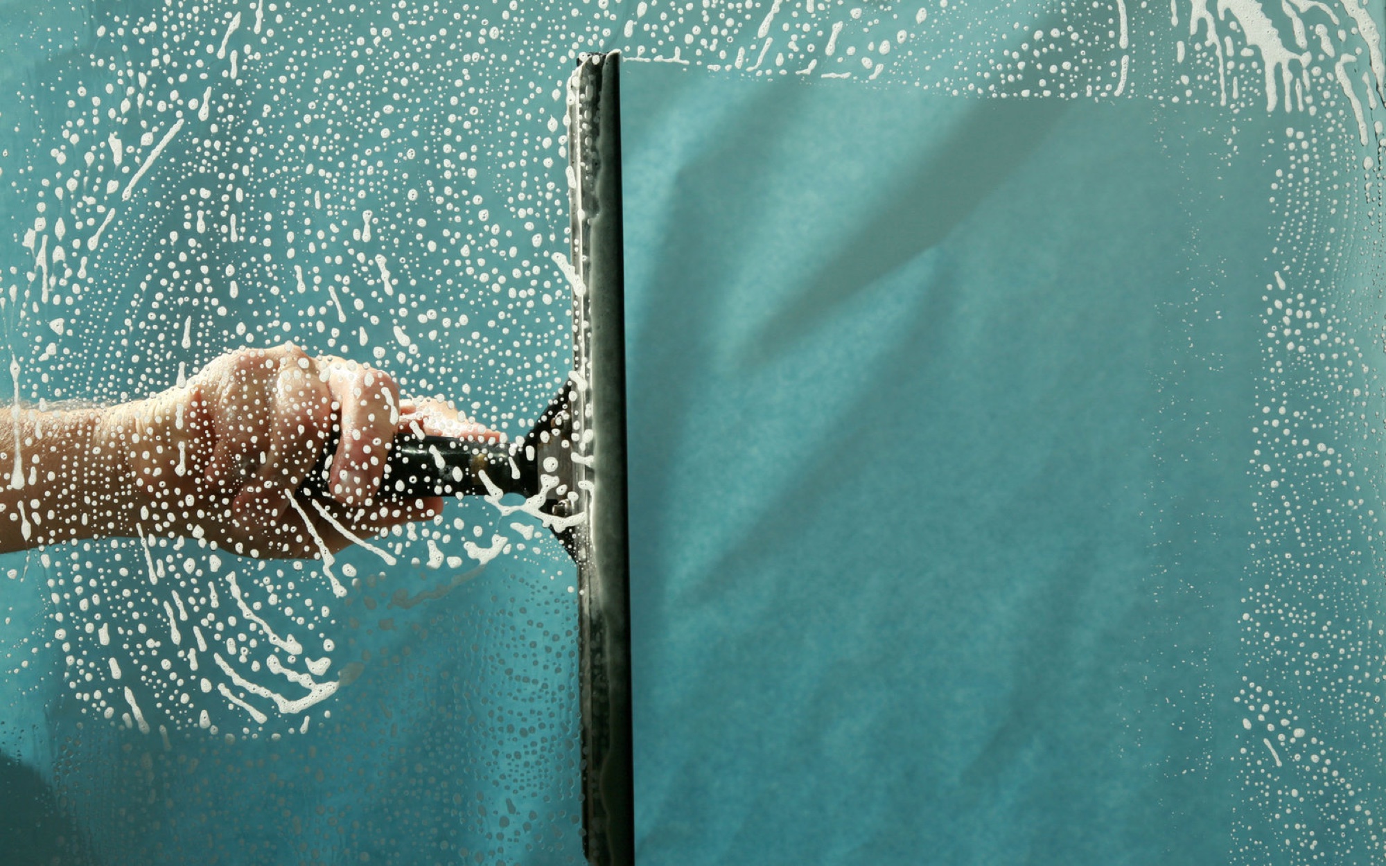 Squeegee clearing a soapy pane of glass — hand window cleaning